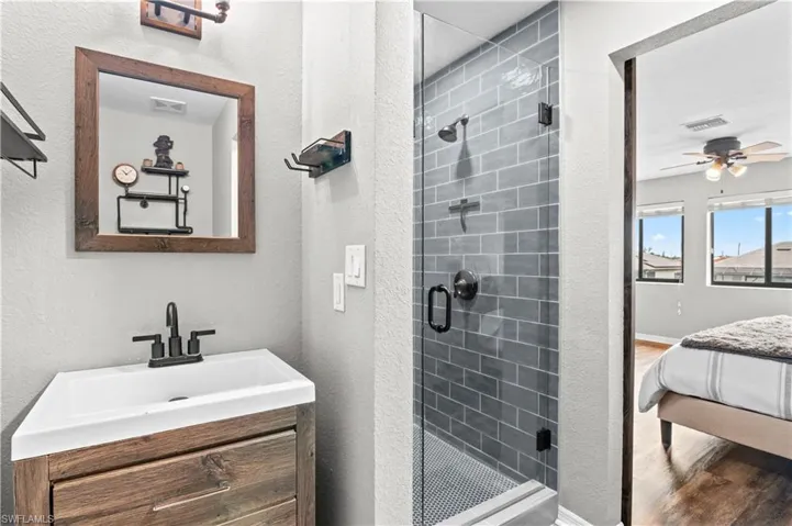 Ensuite bathroom featuring a textured wall, a stall shower, vanity, a ceiling fan, and wood finished floors