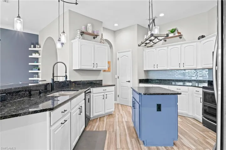 Kitchen featuring white cabinetry, decorative light fixtures, dark stone countertops, light wood-style floors, and backsplash