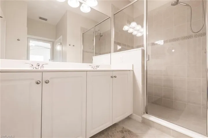 Bathroom with double vanity, a shower stall, and light tile patterned floors