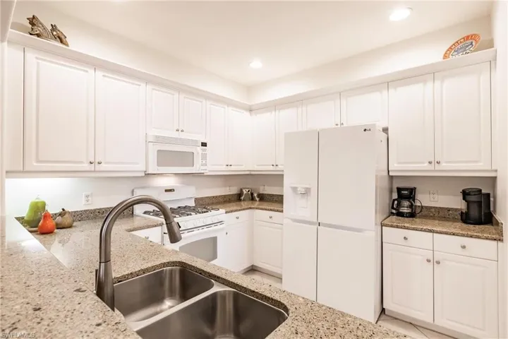 Kitchen featuring white cabinetry, white appliances, light stone counters, and recessed lighting