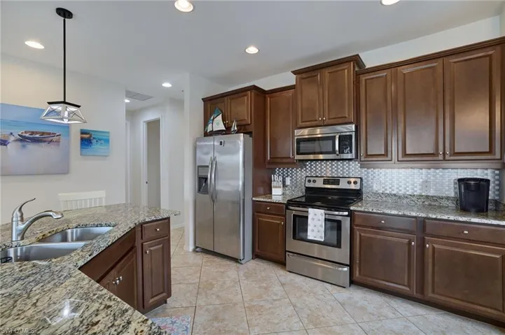Kitchen featuring light stone countertops, stainless steel appliances, tasteful backsplash, a sink, and decorative light fixtures