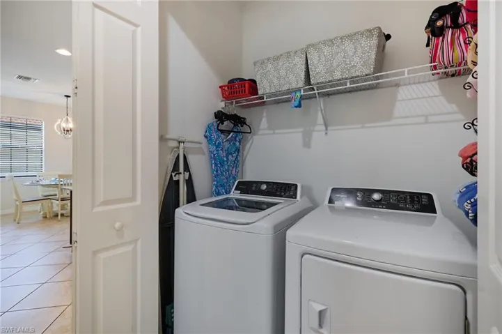 Laundry room with an inviting chandelier, separate washer and dryer, light tile patterned flooring, visible vents, and laundry area