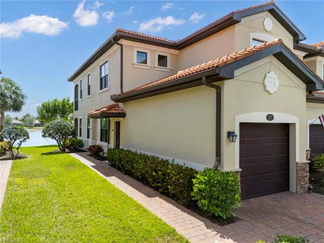 View of property exterior with stucco siding, a tiled roof, a water view, driveway, and a yard