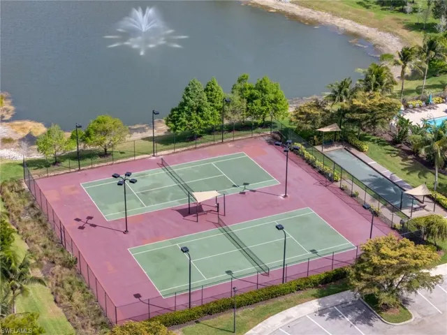 View of tennis court with a water view and fence