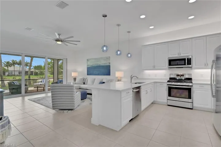 Open-concept living area featuring a white kitchen with stainless steel appliances, a center island with sink, and pendant lighting