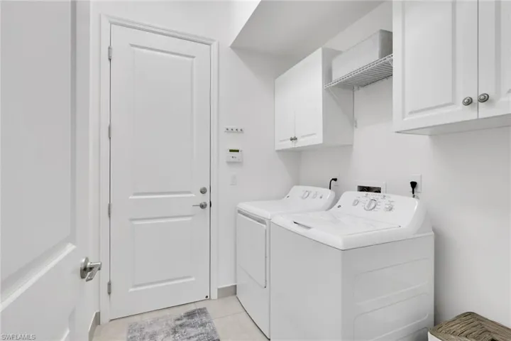 Dedicated laundry area featuring white cabinetry, an open wire shelf, and light-toned tile flooring