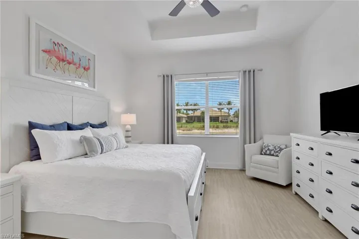 Spacious room featuring wood-finish flooring, a tray ceiling with a ceiling fan, and a large window with horizontal blinds
