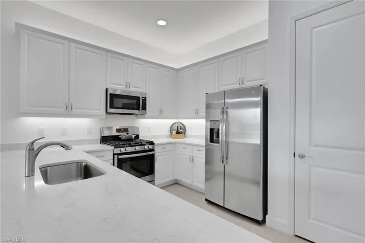 Modern kitchen featuring white shaker cabinetry, stainless steel appliances, light-toned countertops, a stainless steel sink with a gooseneck faucet, and recessed lighting