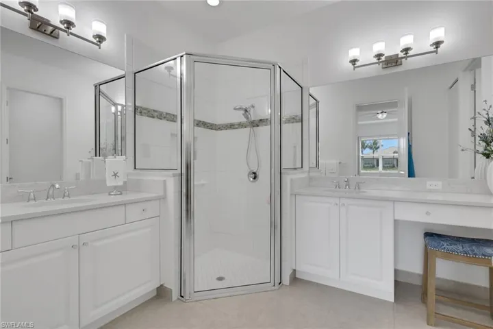 Bathroom featuring a glass-enclosed shower with decorative accent tile, dual vanity sinks, white cabinetry, and a dedicated vanity area