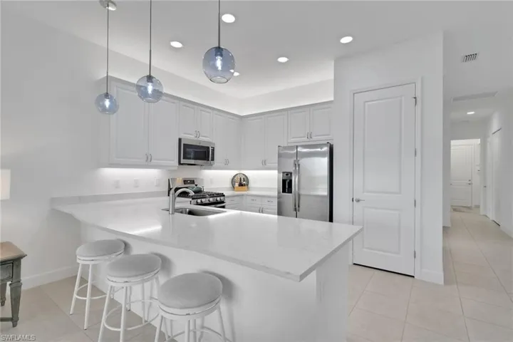 Modern kitchen featuring white shaker cabinetry, stainless steel appliances, a white solid surface countertop, and three spherical pendant lights