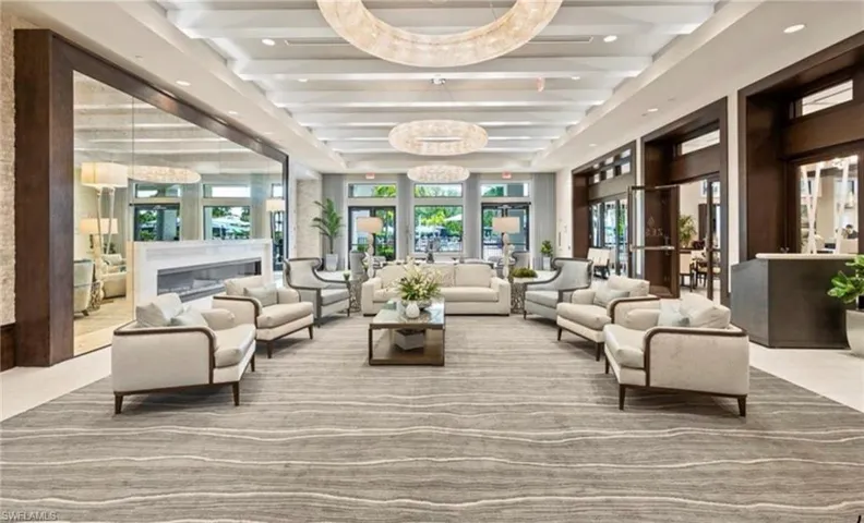 Spacious common area featuring a coffered ceiling with multiple circular chandeliers, a built-in linear fireplace with a stone surround, an expansive area rug, and wood-paneled walls
