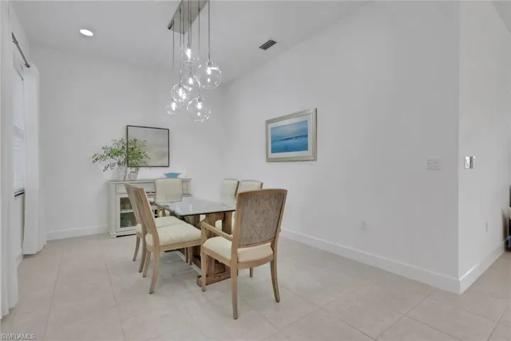 Dining area featuring a contemporary chandelier with multiple glass globes, tile flooring, and crisp white walls