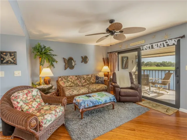 Living area fully furnished featuring a ceiling fan and balcony view overlooking the golf course and pond.