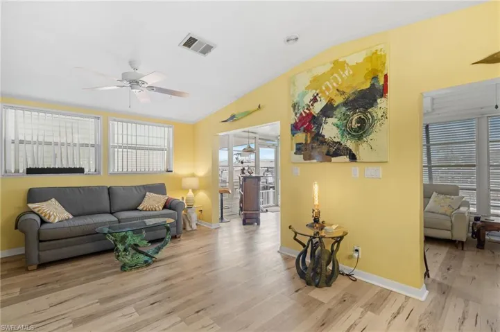 Living room with light wood-type flooring, vaulted ceiling, ceiling fan, and ornamental molding