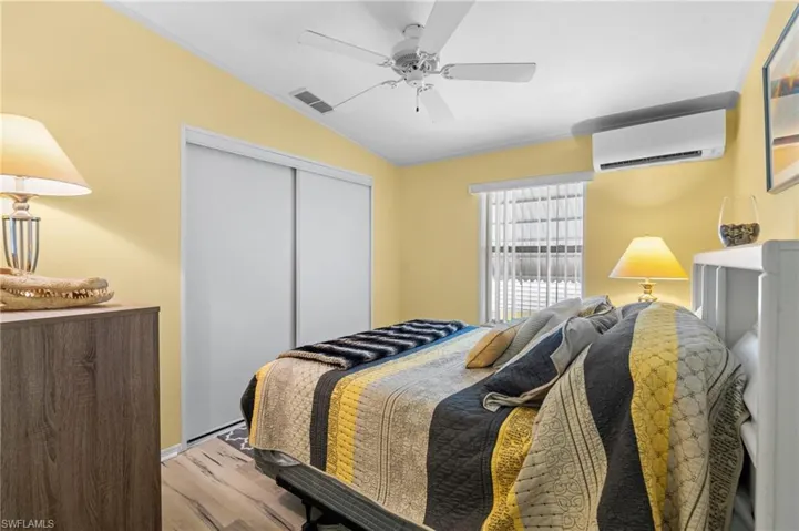 Bedroom with a wall mounted air conditioner, light wood-type flooring, vaulted ceiling, ceiling fan, and a closet