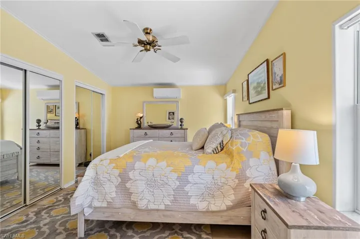 Bedroom featuring an AC wall unit, vaulted ceiling, ceiling fan, and multiple closets