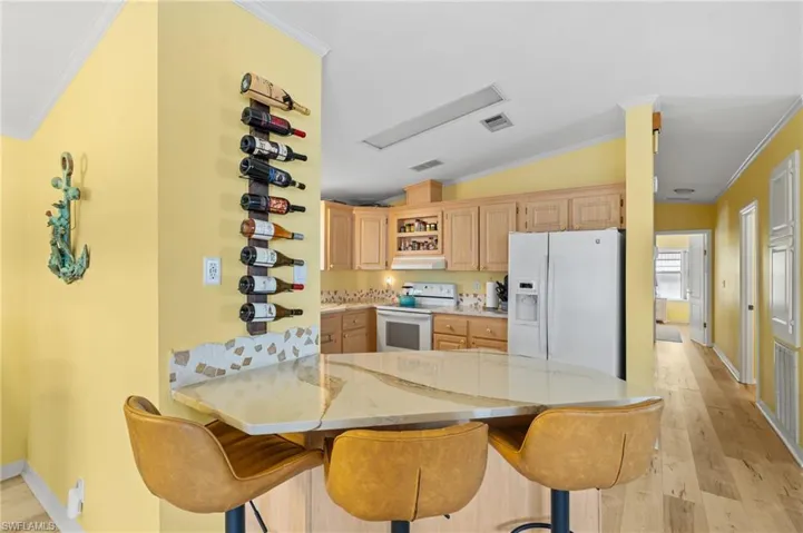 Kitchen with a kitchen bar, quartz counters, white appliances, kitchen peninsula, and light brown cabinetry