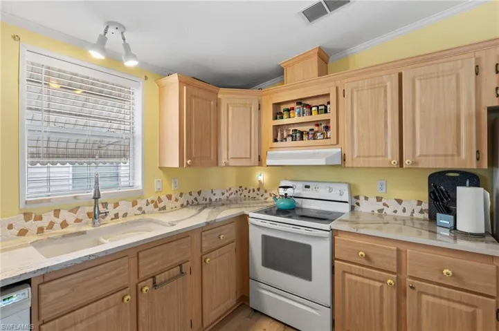 Kitchen with sink, light brown cabinets, light stone counters, crown molding, and white appliances