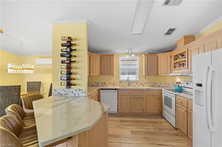 Kitchen with a breakfast bar, light brown cabinets, white appliances, and sink