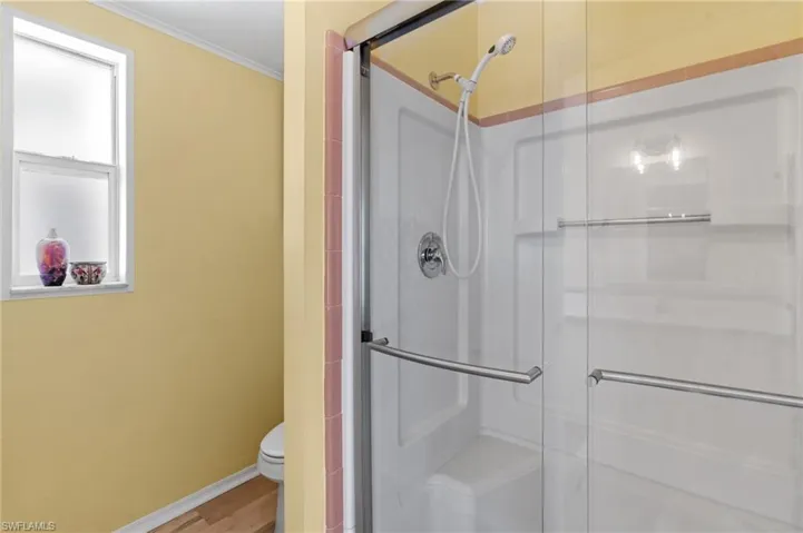 Bathroom featuring light wood-style flooring, toilet, a shower with door, and crown molding