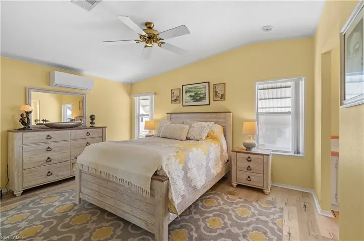 Bedroom with ceiling fan, wood-type flooring, a wall unit AC, and vaulted ceiling