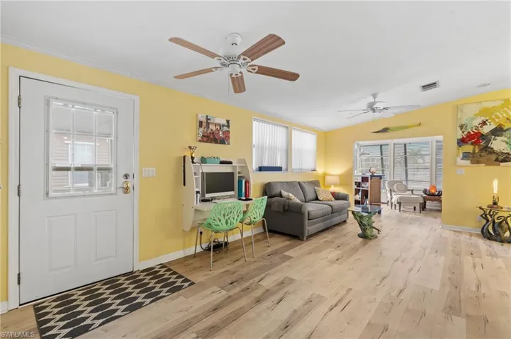 Living room with ceiling fan, vaulted ceiling, ornamental molding, and light wood-style flooring