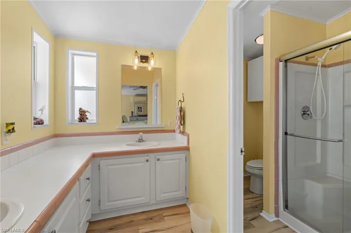 Bathroom featuring crown molding, an glass enclosed shower, toilet, vanity, and light wood-style flooring