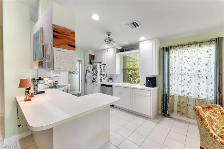 Kitchen featuring light tile patterned floors, a peninsula, white electric range, light countertops, and white cabinetry