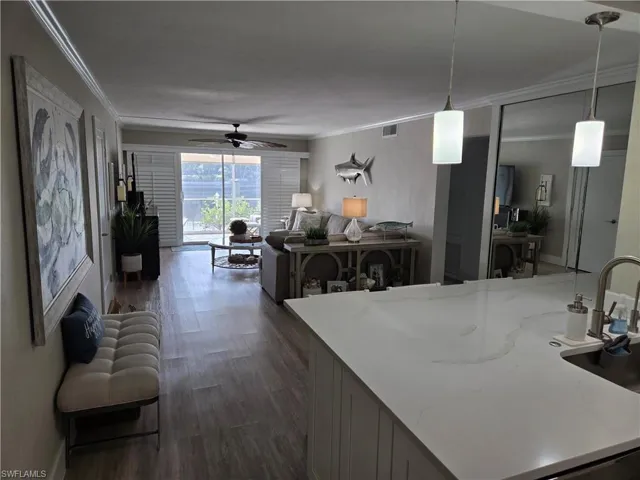 Kitchen with ceiling fan, dark hardwood / wood-style floors, light stone countertops, ornamental molding, and decorative light fixtures