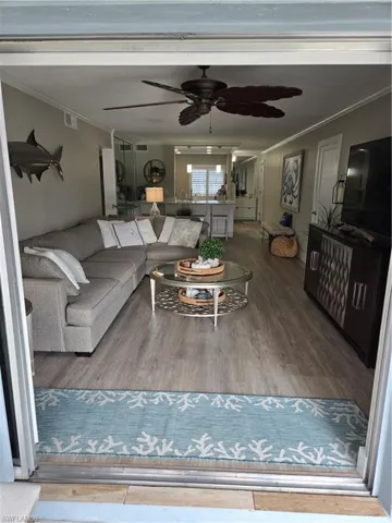 Living room with ceiling fan, ornamental molding, and wood-type flooring