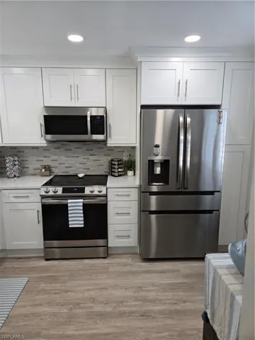 Kitchen featuring range, refrigerator, light hardwood / wood-style floors, and white cabinets