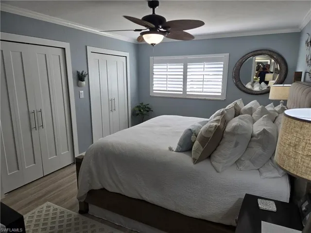 Bedroom featuring ceiling fan, crown molding, wood-type flooring, and multiple closets