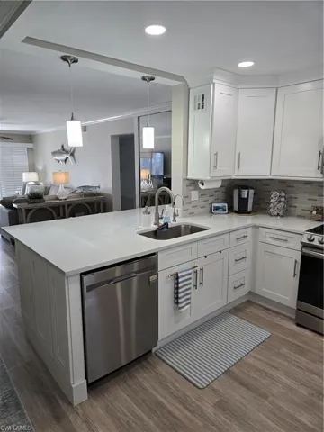 Kitchen with sink, dishwasher, stove, white cabinetry, and kitchen peninsula