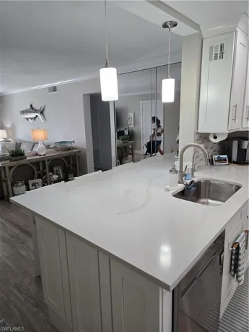 Kitchen with sink, hanging light fixtures, ornamental molding, white cabinets, and dark hardwood / wood-style flooring