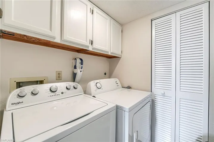 Dedicated laundry area featuring white upper cabinetry, a wood-finish shelf, and louvered bi-fold doors