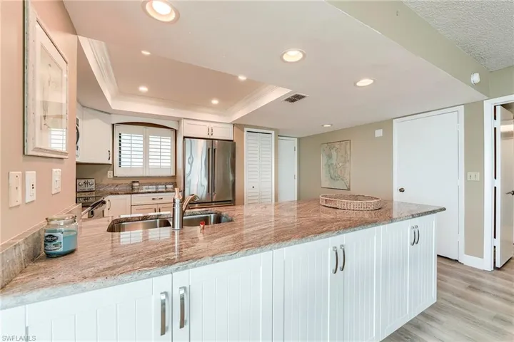 Expansive kitchen island featuring a dual-basin stainless steel sink with a gooseneck faucet, light-toned stone countertop, and white shaker-style cabinetry with chrome hardware