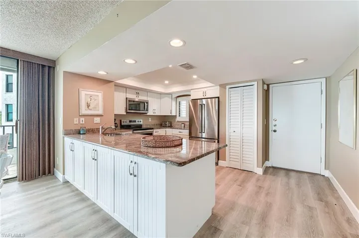 Open-concept kitchen featuring white cabinetry, stone countertops, stainless steel appliances, recessed lighting, and wood-finish flooring