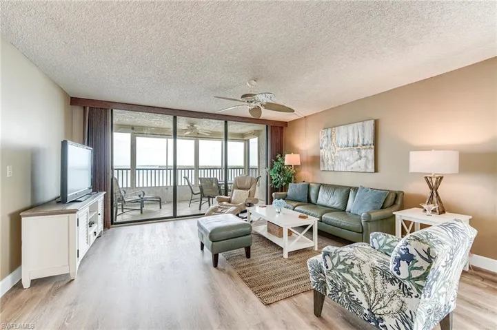 Living area featuring wood-finish flooring, neutral wall tones, and floor-to-ceiling glass doors opening onto a balcony