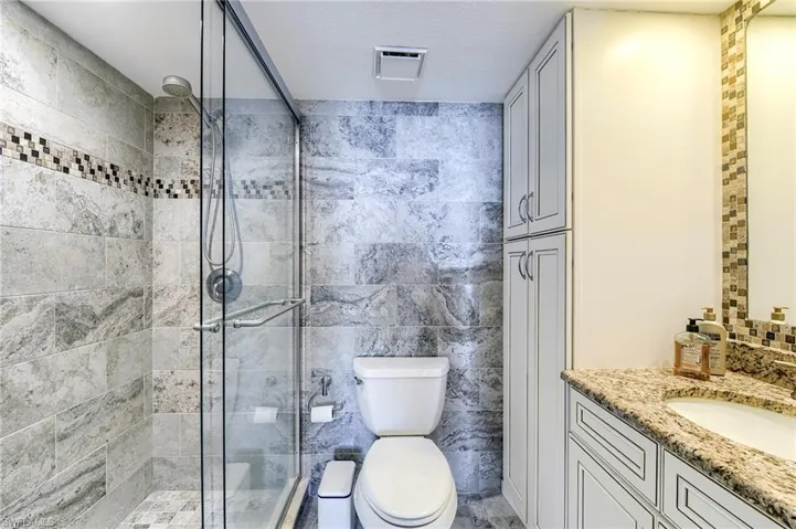 Bathroom featuring a glass-enclosed shower with patterned tile accents, a toilet, and full-height cabinetry