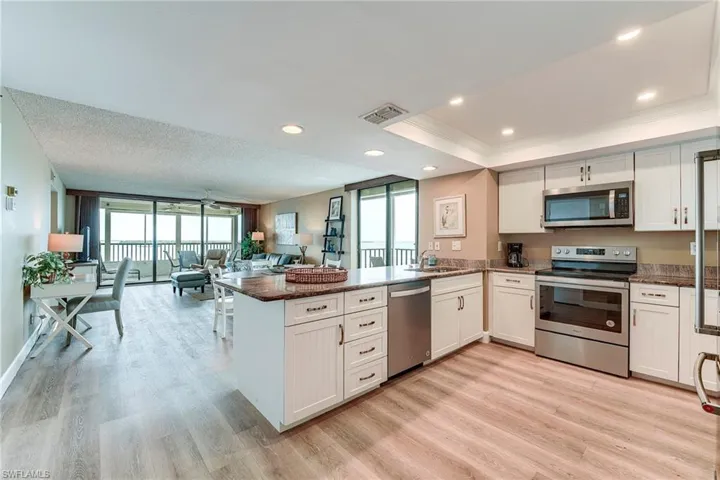 Open-concept kitchen featuring white shaker-style cabinetry, stainless steel appliances, and a central island with a stone countertop