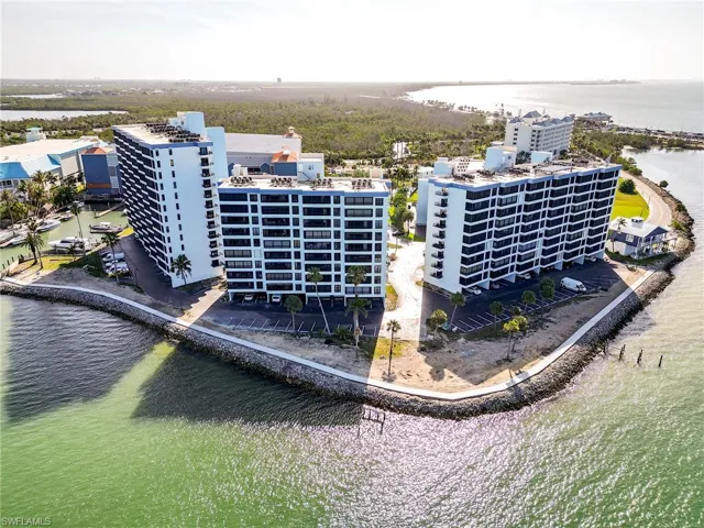 Waterfront condominium buildings with multiple balconies, a surrounding seawall, and on-site parking