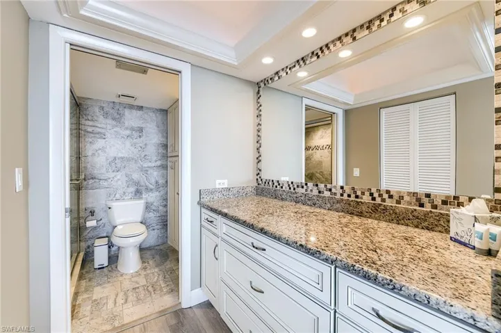 Bathroom vanity with granite countertop and integrated sink, complemented by a tiled backsplash and overhead recessed lighting