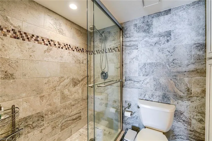 Glass-enclosed shower with a mosaic tile accent band and neutral-toned wall tiles