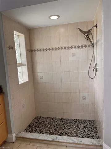 Tiled shower enclosure featuring a pebble mosaic floor, recessed lighting, and a multi-function shower head