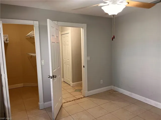 Bedroom featuring neutral wall tones, tile flooring, a ceiling fan with light fixture, and a walk-in closet with shelving