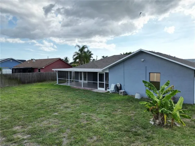 Expansive green lawn featuring a screened-in patio, mature palm tree, and a partial wood fence
