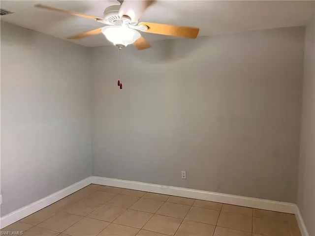 Room featuring a ceiling fan with light fixture, neutral wall paint, white baseboards, and square tile flooring