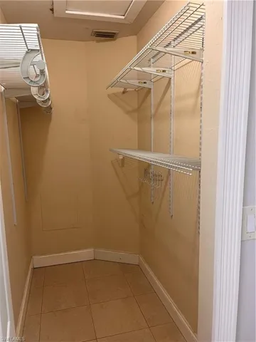 Walk-in closet featuring floor-to-ceiling wire shelving, built-in hanging rods, tile flooring, and a ceiling-mounted access panel