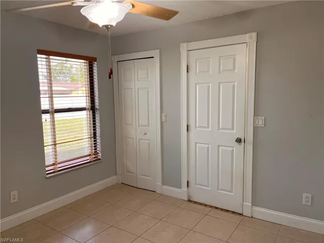 Neutral wall paint finish, ceiling fan with light fixture, window with wood-finish blinds, tile flooring, and white trim