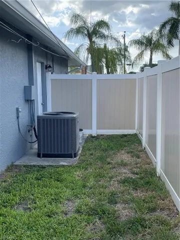 Side yard featuring a tan and white privacy fence, an exterior door with an attached light fixture, and an air conditioning unit on a concrete pad